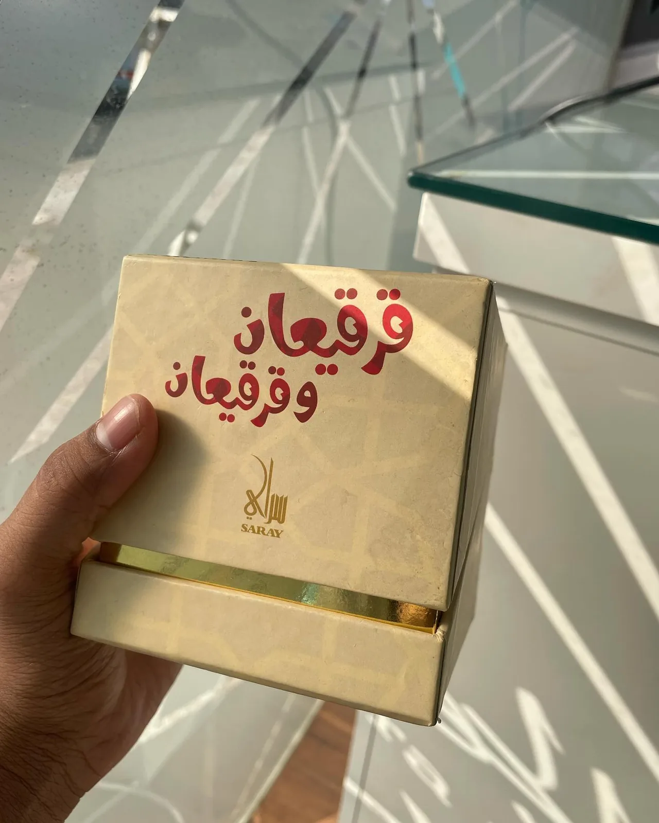 Hand holding a gold-edged gift box with Arabic foil lettering